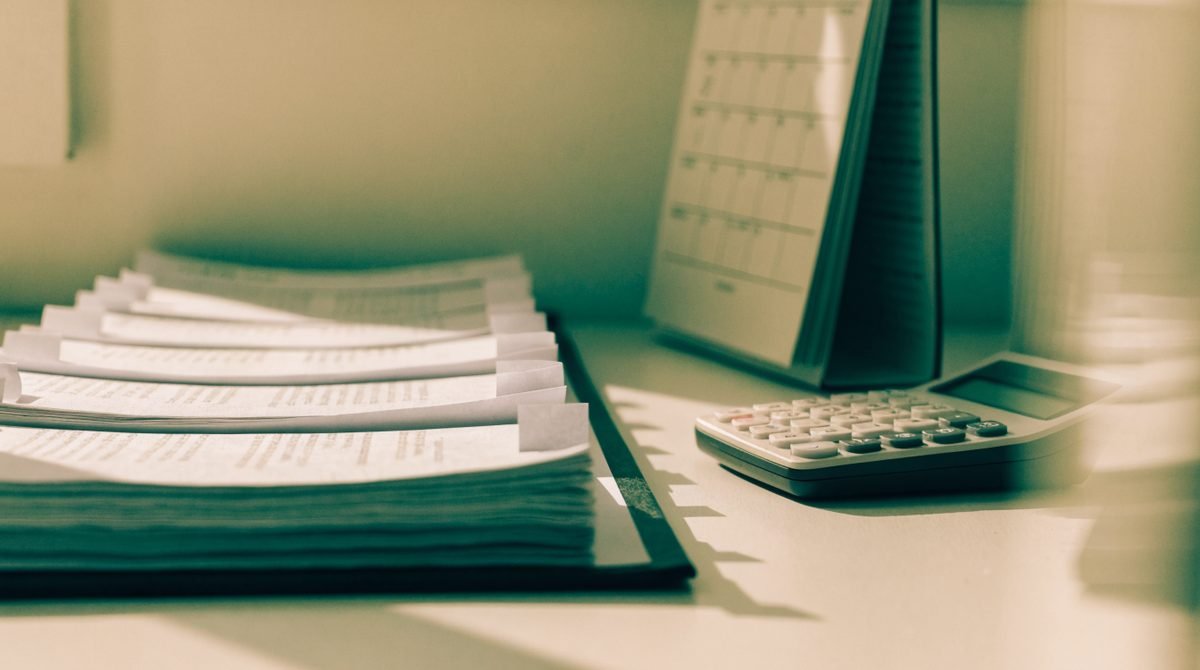 Documentos organizados em pasta aberta ao lado de calendário de parede e calculadora